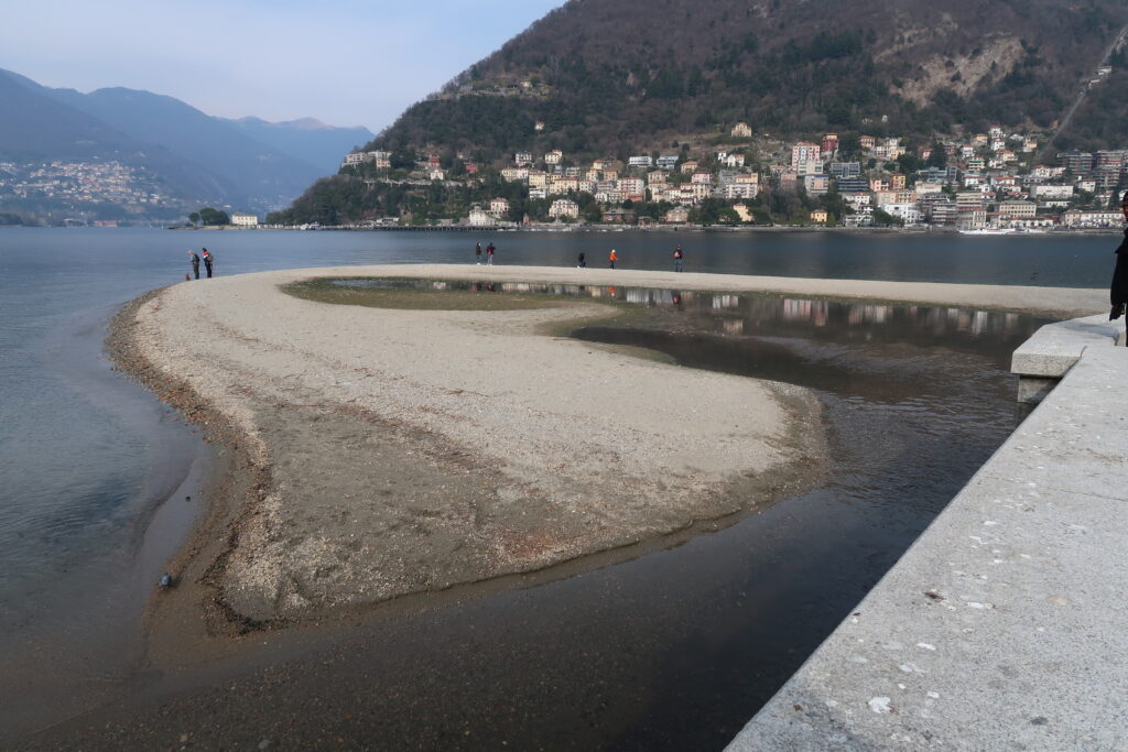 (Como. La spiaggia del Cosia vista dalla foce dell’omonimo torrente. In secondo piano la zona di viale Geno; a sinistra, in fondo, Cernobbio. Fotografia © di Susanna Pagani).